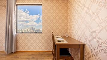 A dining area with a wooden table set for two, a window with a cityscape view, patterned wallpaper, and a wooden floor.