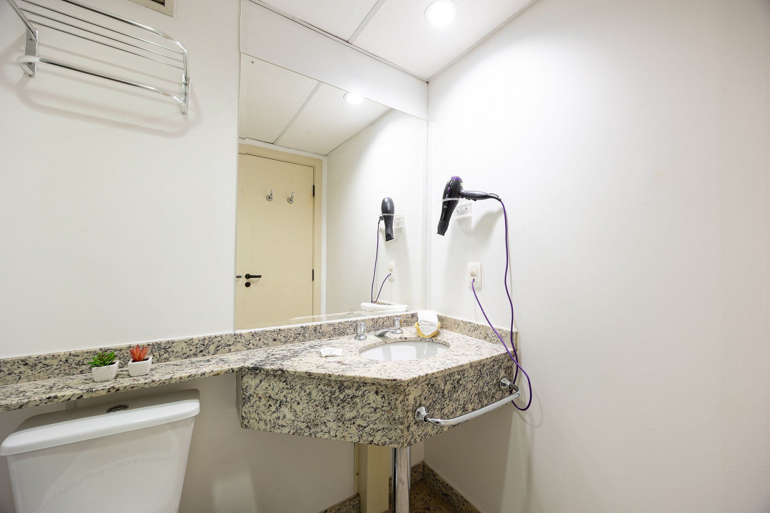 A bathroom with a granite countertop sink, a towel rack, a hairdryer, and a mirror.