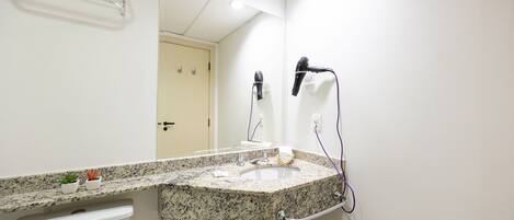 A bathroom with a granite countertop sink, a towel rack, a hairdryer, and a mirror.