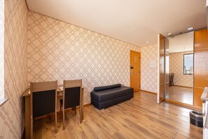 A room with a wooden floor, a sofa, a dining table with chairs, and a patterned wallpaper. - Flat Osasco Trade (Osasco)