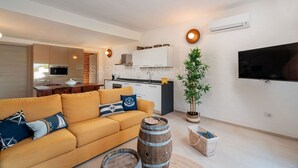 Ein modernes Wohnzimmer mit einer Couch, einem Fernseher und einer Küchenzeile im Hintergrund.