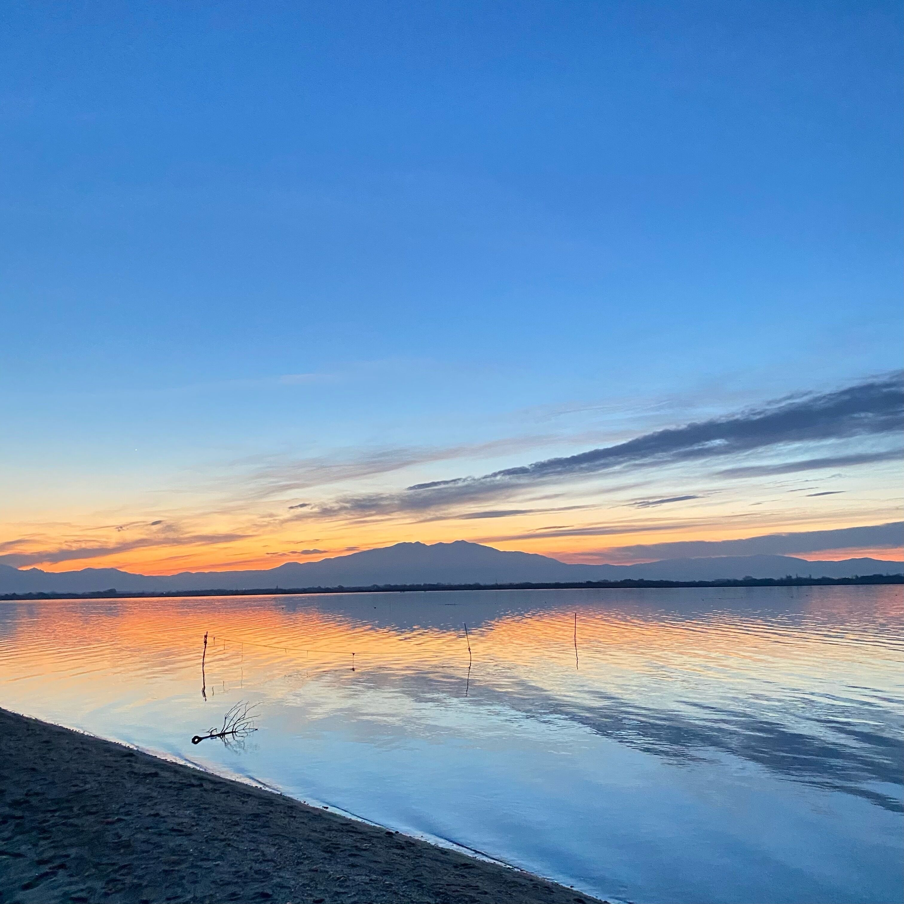 Un lac paisible au coucher du soleil, avec des montagnes en arrière-plan.