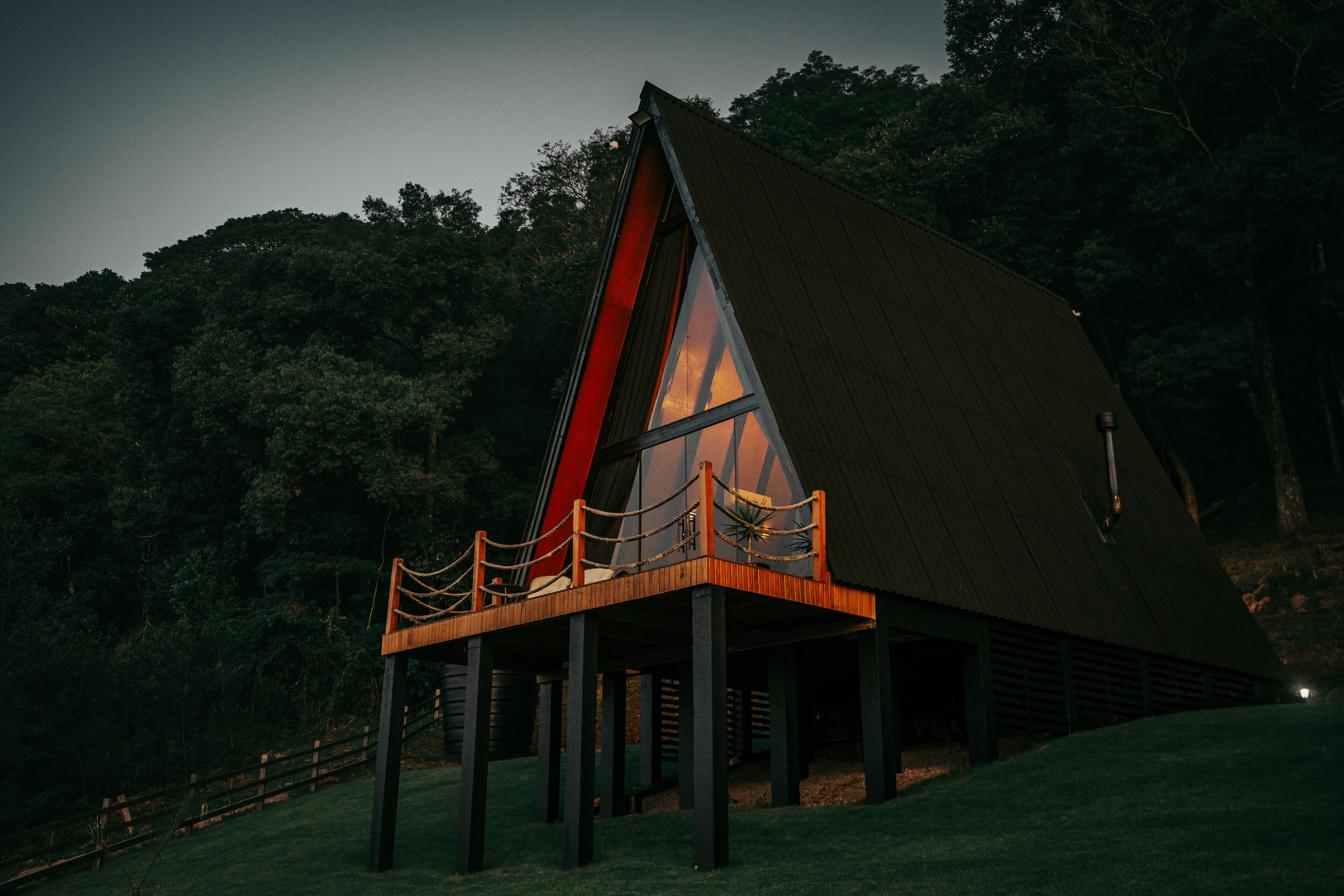 A modern, triangular-shaped building with a wooden deck and a glass facade, surrounded by a forested area.