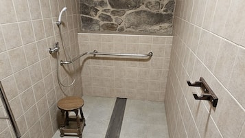 Un baño pequeño con azulejos, que incluye un inodoro, un taburete de madera, una ducha y un pasamanos.