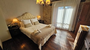 Een slaapkamer met een groot bed, twee nachtkastjes, een kroonluchter en een stenen muur.