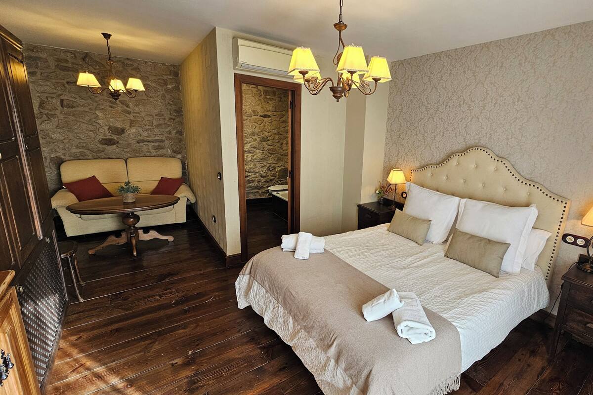 Een hotelkamer met een groot bed, een zithoek met een sofa en fauteuil, een houten vloer en een stenen muur.
