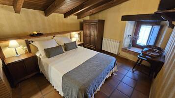 Un dormitorio con una cama grande, cabecero de madera, mesitas de noche con lámparas, un armario de madera, un radiador y una ventana con vistas.