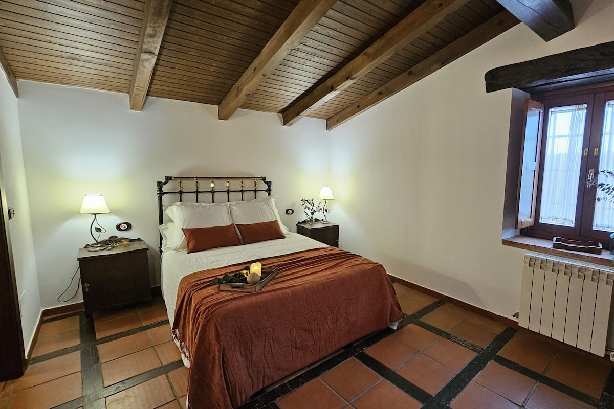 Een slaapkamer met een bed, twee nachtkastjes, een raam met uitzicht en een radiator.