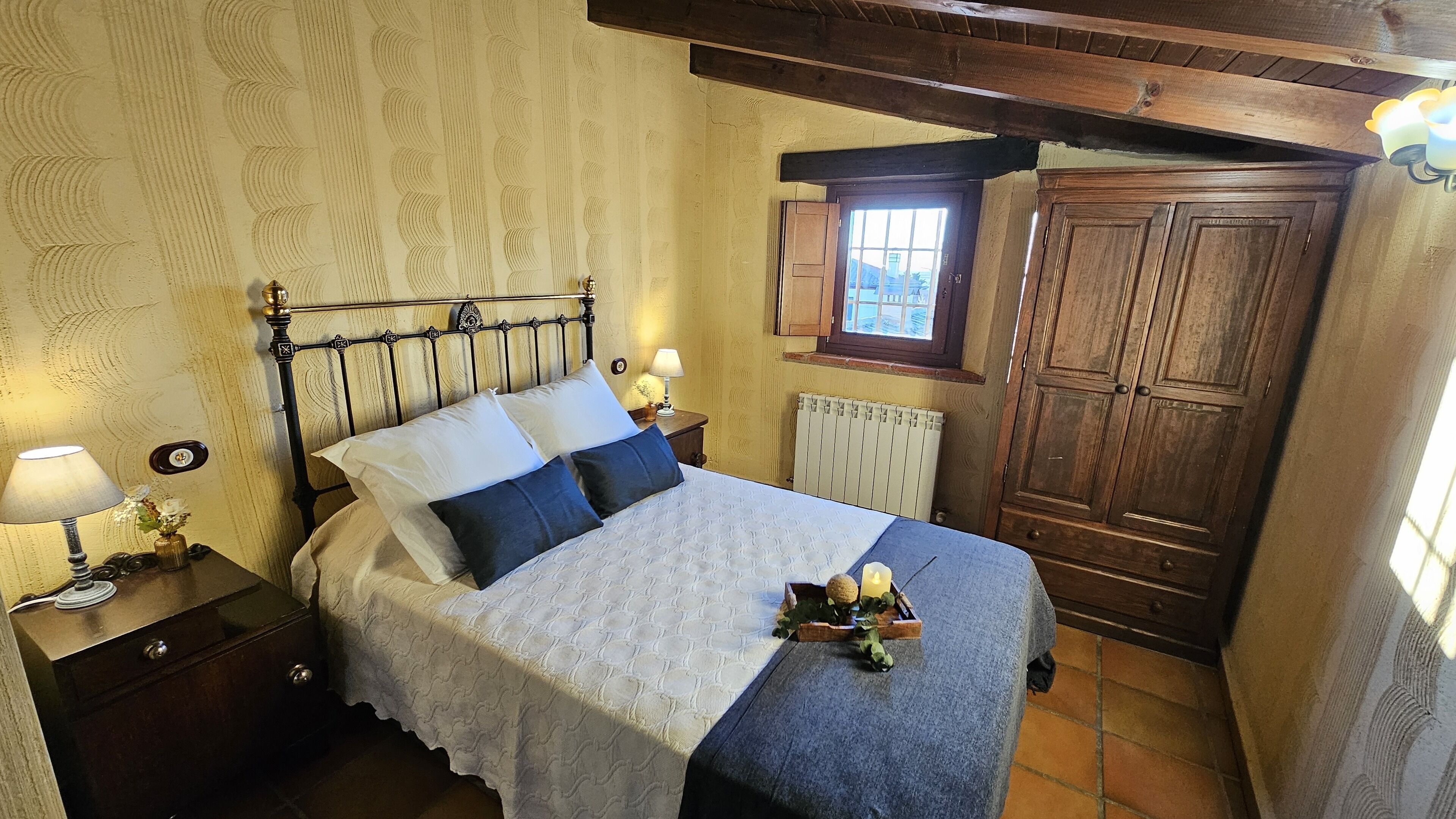 A bedroom with a bed, nightstands, a wooden wardrobe, and a window with a view.
