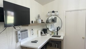 Eine kleine Küche mit Flachbildfernseher, Spüle, Spiegel und Kaffeemaschine.