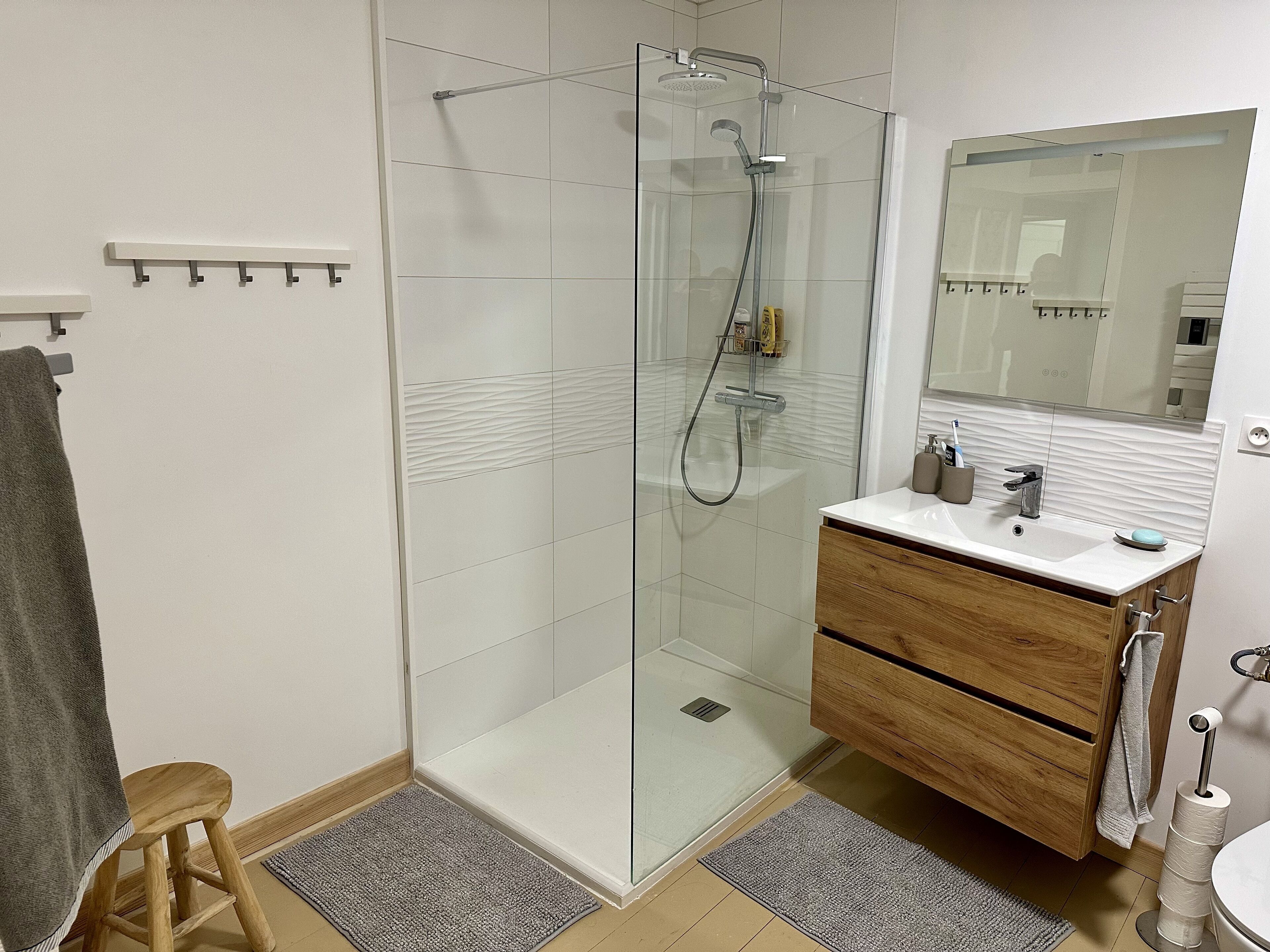 A modern bathroom with a glass shower enclosure, a wooden vanity, and a large mirror.