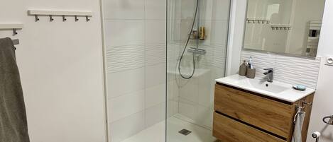 A modern bathroom with a glass shower enclosure, a wooden vanity, and a large mirror.