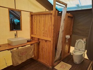 A compact bathroom with a wooden door, a sink, a mirror, and a toilet. - TAYARI LUXURY TENTED CAMP- MASAI MARA (Maasai Mara)