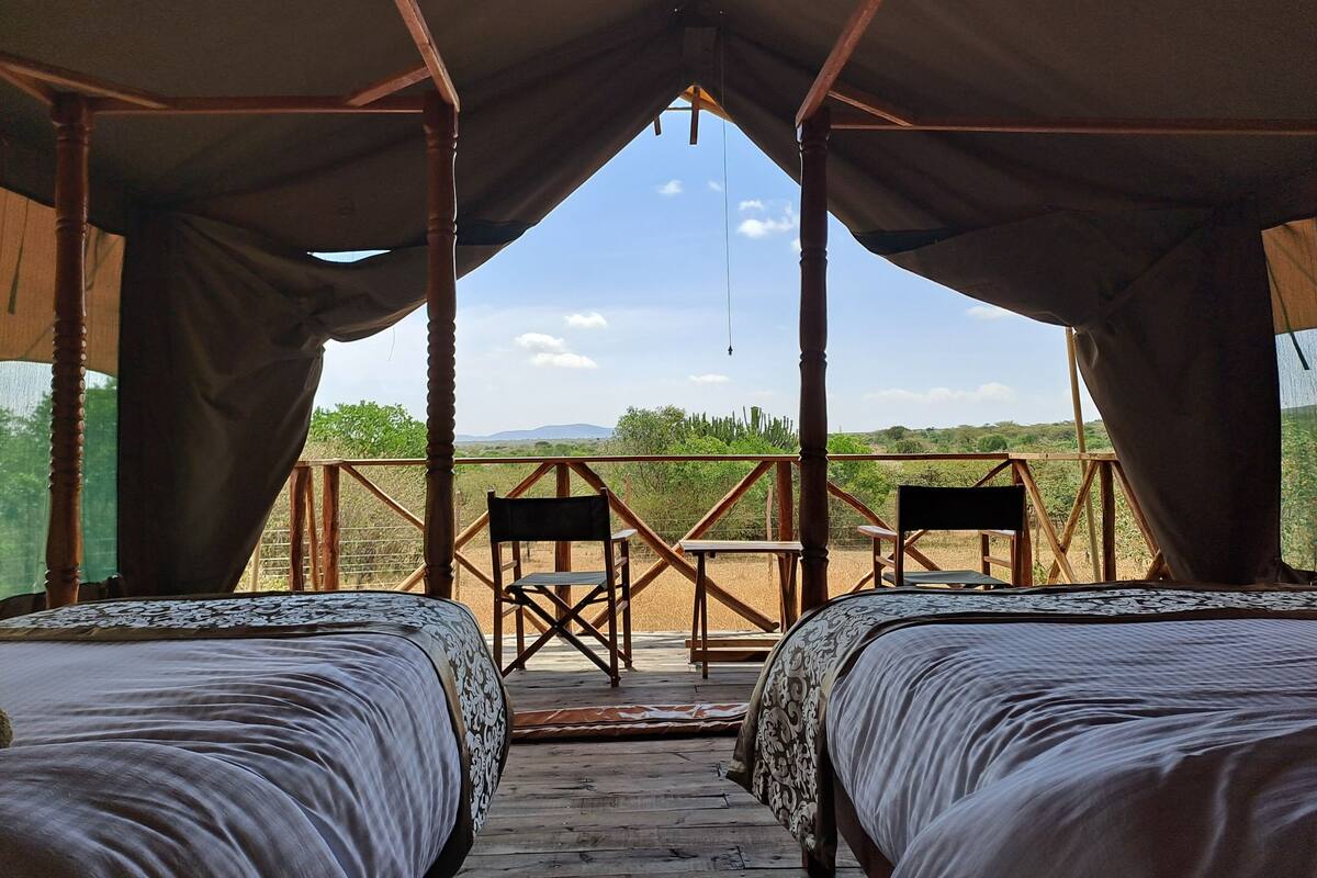 A tented accommodation with two beds, a wooden deck, and a view of the landscape.