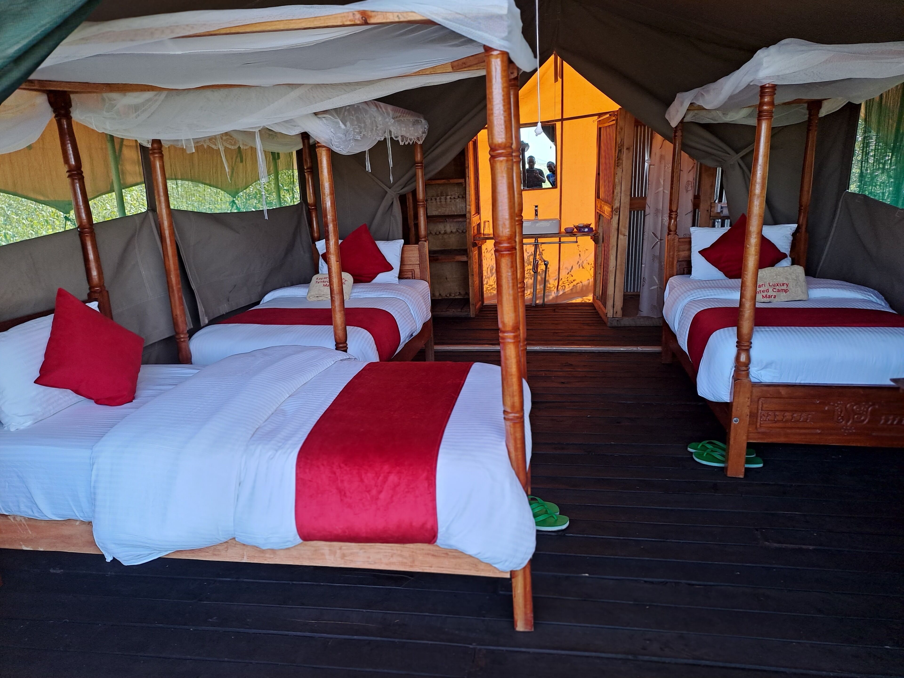 A series of four wooden four-poster beds with white and red bedding, arranged in a row under a canopy.