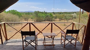 Een houten terras met twee stoelen en een tafel, met uitzicht op een droog landschap met schaarse begroeiing en heuvels in de verte.