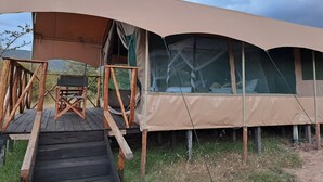 Een tentaccomodatie met een houten terras, een bed met hemelbed en uitzicht op het omliggende landschap.