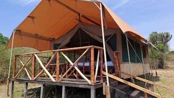 Une tente de safari dotée d’une terrasse en bois et d’un lit simple.