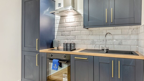 Une cuisine moderne avec des meubles de couleur gris foncé, un pare-feu en marbre et un évier en acier inoxydable.