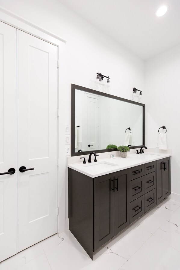Un baño moderno con lavamanos doble, armarios oscuros y un espejo grande.