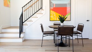 Un escalier avec une rampe noire, une table à manger avec quatre chaises et une plante en pot.