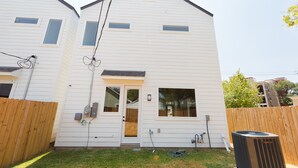 Une maison à deux étages avec une porte d’entrée, deux fenêtres et un tableau électrique visible.