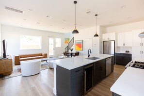 Una cocina moderna con una isla central, electrodomésticos de acero inoxidable y un comedor con sofá y sillas.