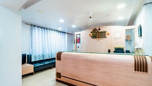 A hotel room with a wooden bed, a sofa, a small table, and a ceiling fan. - Itsy Hotels Anupam (Mahabaleshwar)