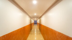 A long, narrow hallway with white and orange walls, a shiny floor, and a blue door at the end. - Itsy Hotels Anupam (Mahabaleshwar)