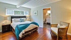 Ein Schlafzimmer mit einem Bett, Nachttischen, einem Sessel, einem Fenster und einer Tür zu einem Badezimmer.