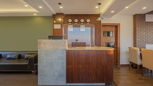 A reception desk with a wooden finish, a seating area with a sofa and chairs, and a wall with clocks showing different time zones. - Treebo The Northern Retreat Resort With Mountain View (Kumharsain)