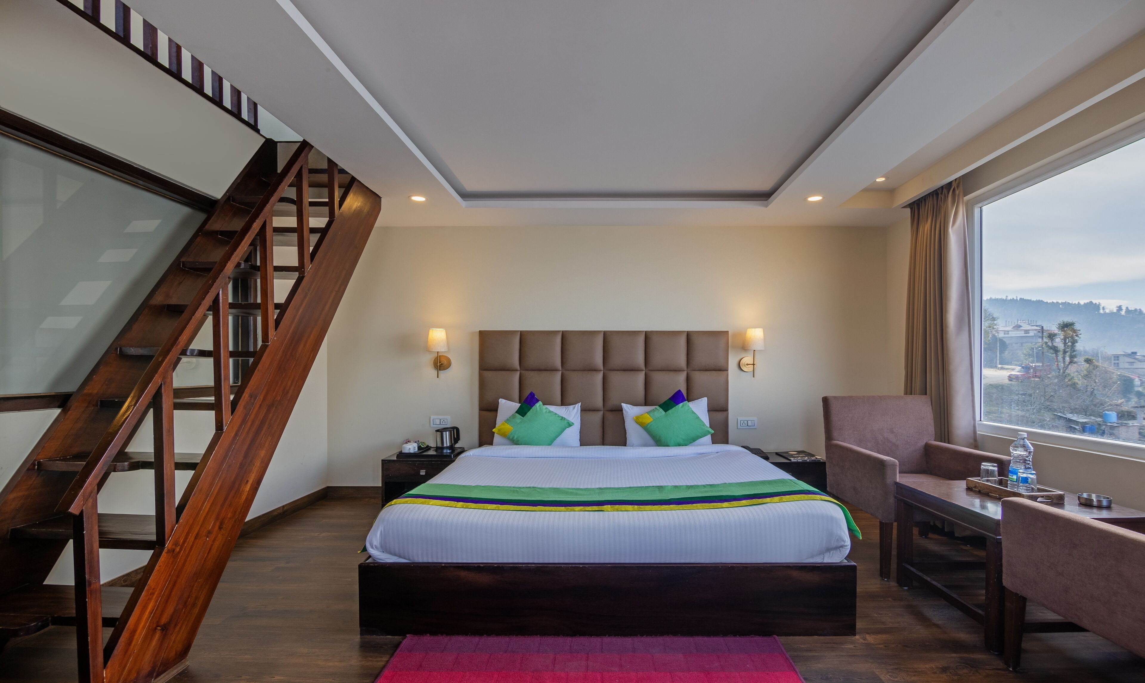 A hotel room with a bed, a desk, a chair, a staircase, and a view of the city.