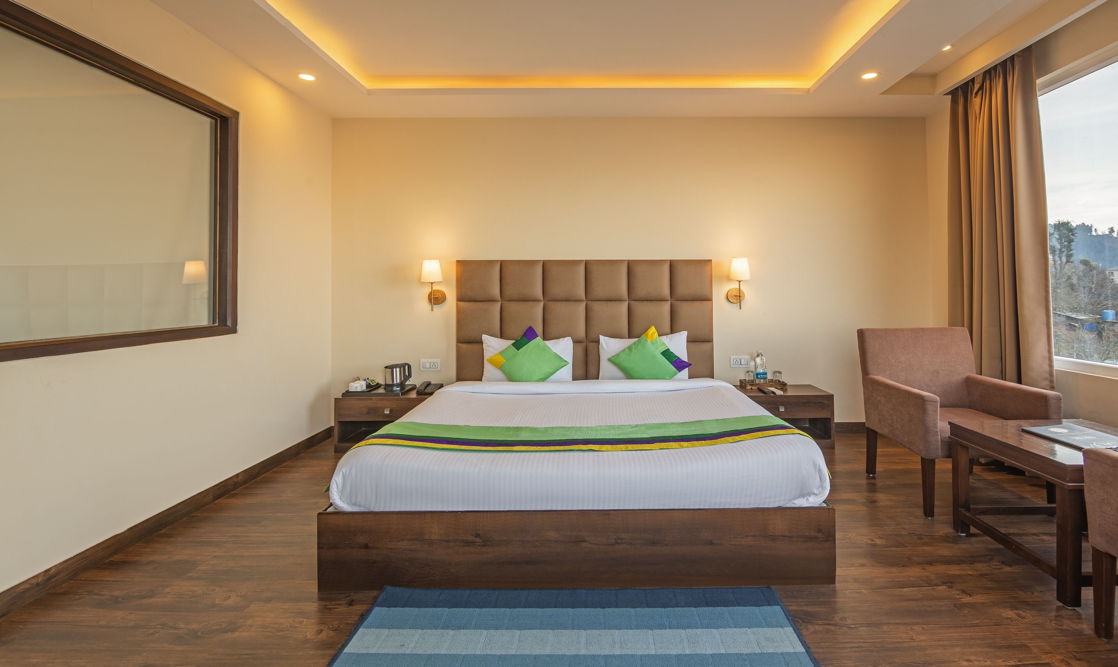 A hotel room with a large bed, two bedside tables, a chair, a desk, and a view of the outside.