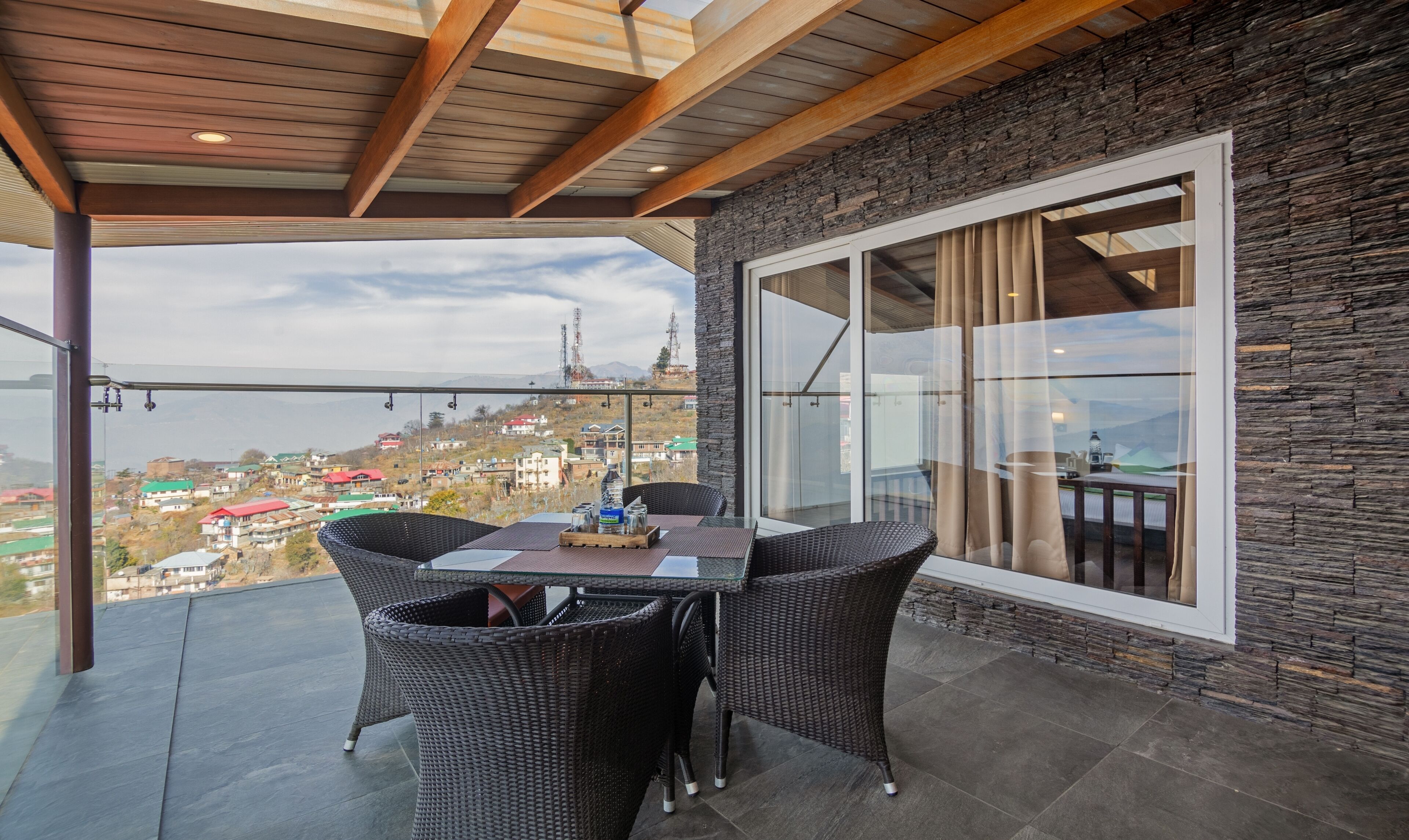 Uma varanda com móveis de vime, uma mesa e vista para uma cidade.