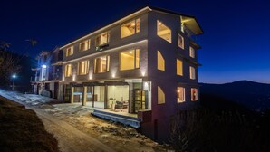 A multi-story hotel with a modern design, featuring large windows and a well-lit entrance. - Treebo The Northern Retreat Resort With Mountain View (Kumharsain)
