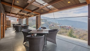 A spacious indoor area with a high ceiling, large windows offering a view of a mountainous landscape. - Treebo The Northern Retreat Resort With Mountain View (Kumharsain)