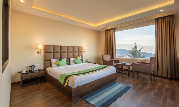 A hotel room with a large bed, a desk, and a chair. There is a window with a view of mountains. - Treebo The Northern Retreat Resort With Mountain View (Kumharsain)