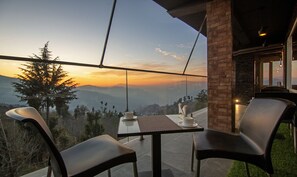 A terrace with a table and chairs, overlooking a mountainous landscape during sunset. - Treebo The Northern Retreat Resort With Mountain View (Kumharsain)