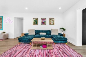Una sala de estar moderna con un sofá seccional color turquesa, una mesa de centro de madera y una alfombra rosa vibrante.