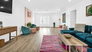 Una sala de estar moderna con piso de madera, un sofá color esmeralda, una mesa de centro de madera y un tapete rosa.
