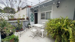 Un patio con una mesa y sillas, rodeado de plantas en macetas y un colgador de luz.