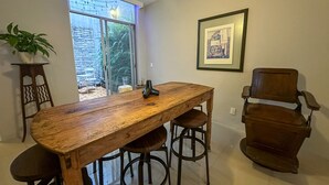 Un comedor con una mesa de madera y taburetes de bar, un cuadro en la pared y vistas a través de un ventanal grande.