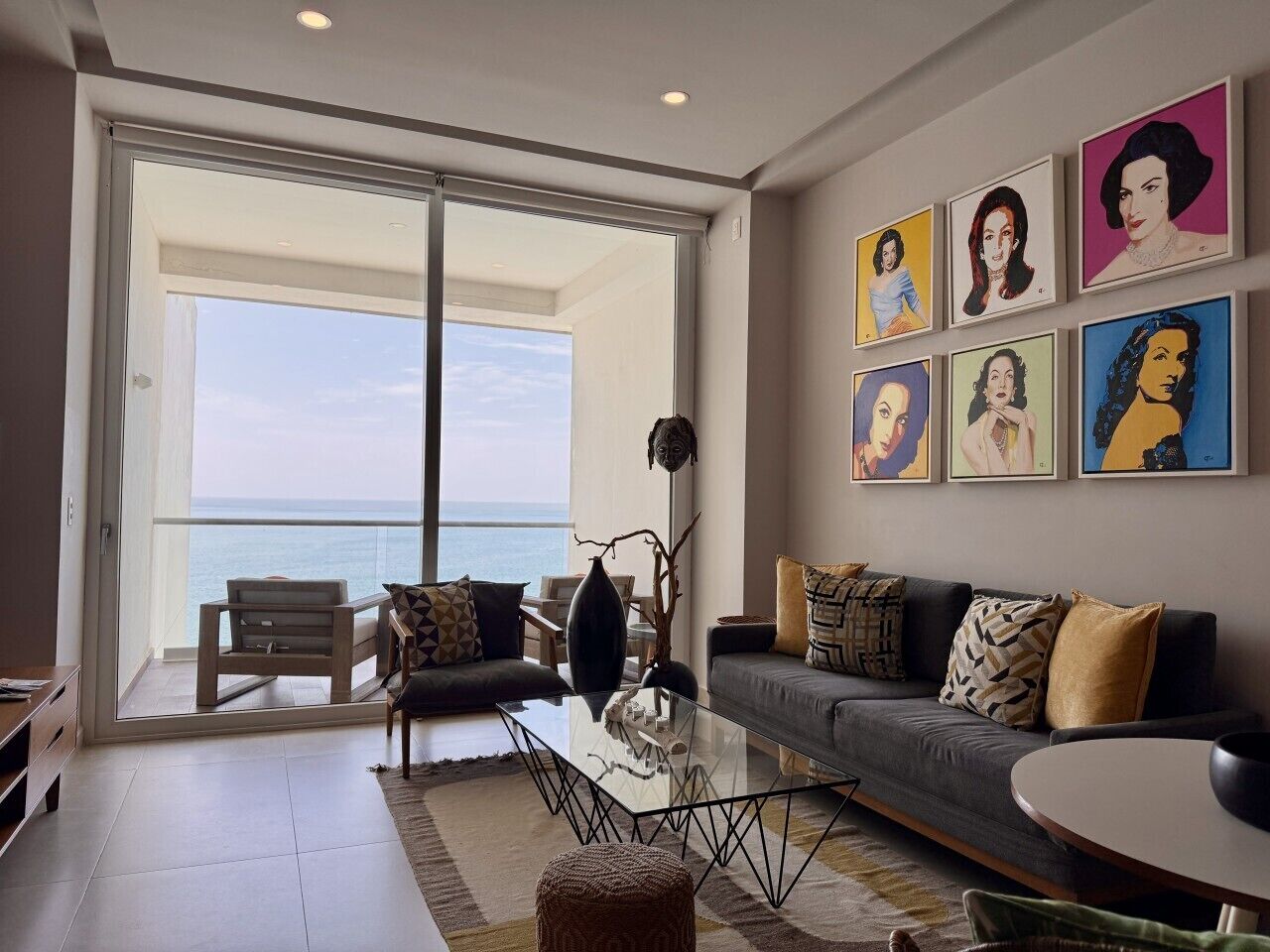 A modern living room with a glass door leading to a balcony, a sofa, a coffee table, and a wall with framed artwork.