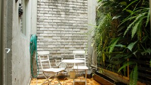 Un petit espace patio agrémenté d’un mur en briques, de deux chaises blanches, d’une petite table ronde et d’une plante en pot.