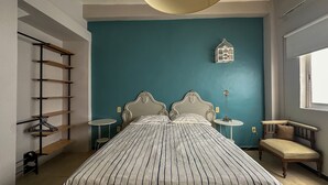 Une chambre à coucher avec un grand lit, deux tables de chevet, une chaise, un luminaire suspendu et une cage à oiseaux fixée au mur.