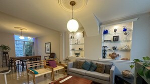 Un salon comprenant un canapé, une table basse et des fauteuils, un coin repas avec une table et des chaises, et une bibliothèque agrémentée d’objets décoratifs.