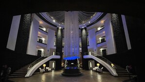 En rymlig entréhall med en central fontän, två trappor och en modern arkitektonisk design.