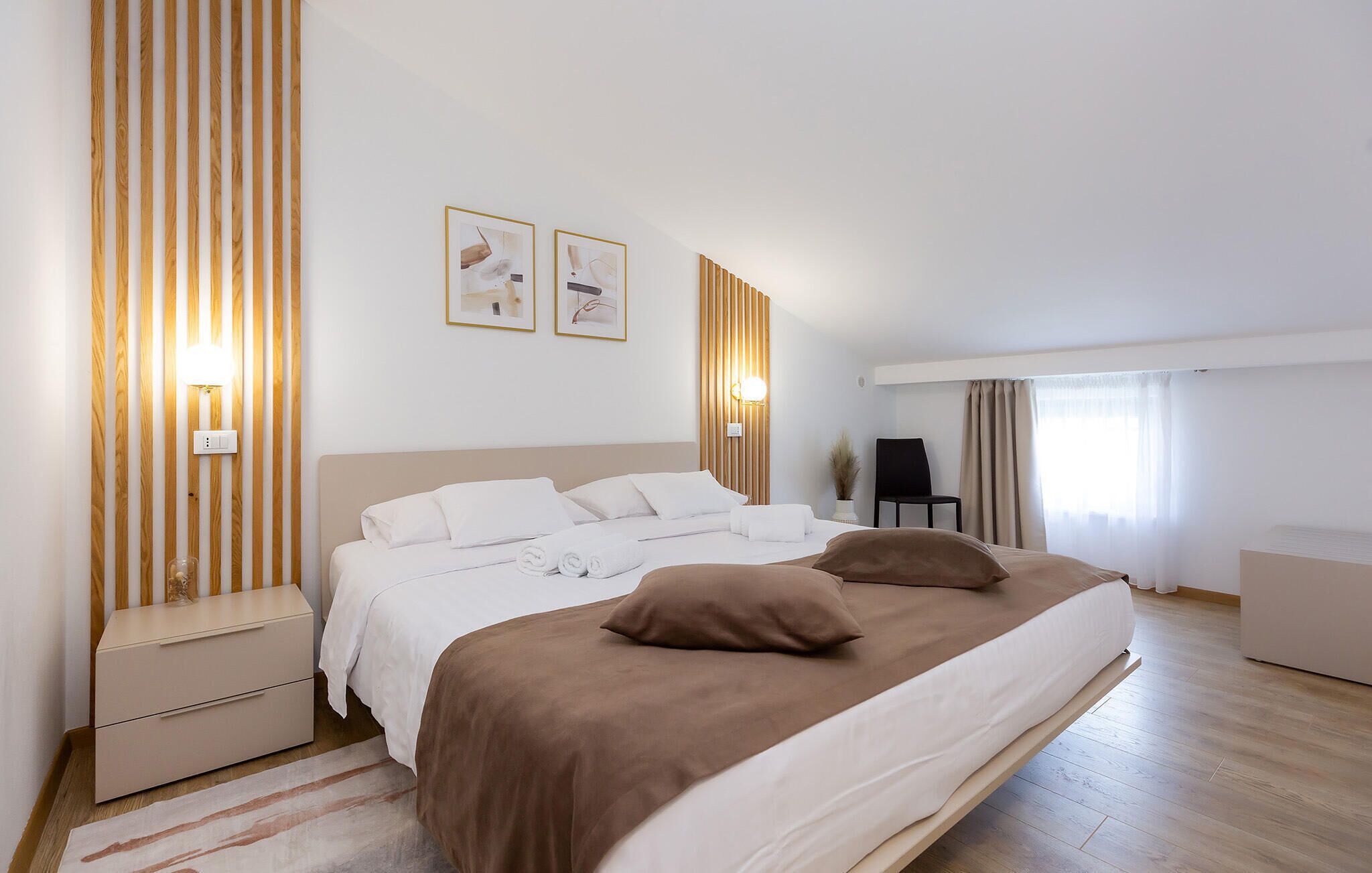A modern hotel room with a large bed, a nightstand, a chair, and a desk.