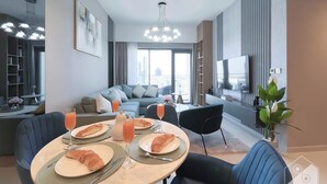Una sala de estar moderna con comedor, que incluye un sofá, un televisor y una mesa de comedor con croissants y vasos de jugo.