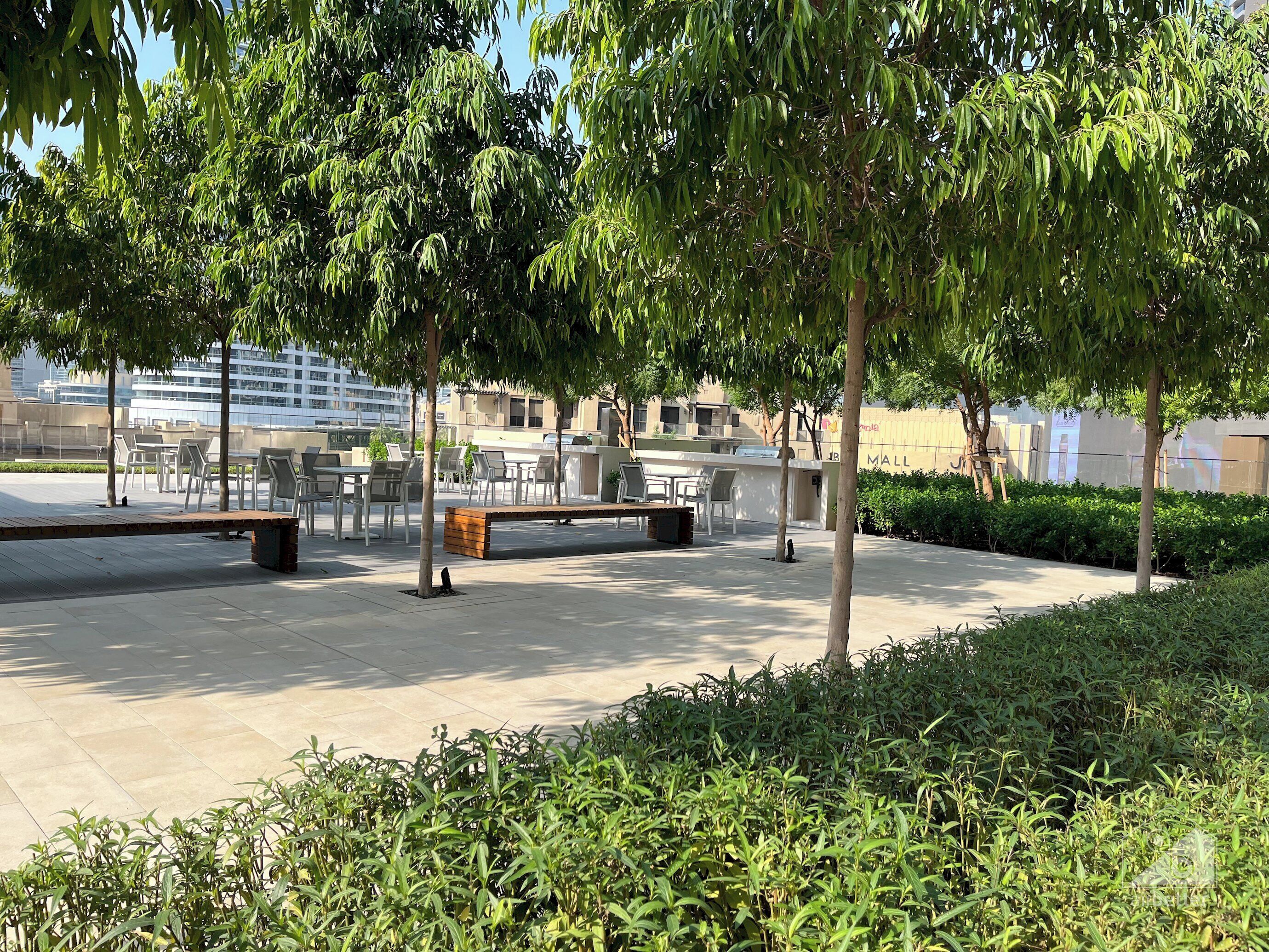 An outdoor seating area with tables and chairs, surrounded by trees and greenery.